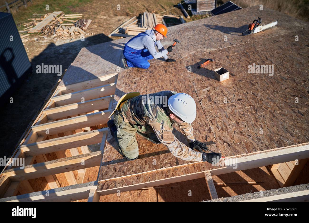 Carpenters hammering nail into OSB panel on the roof top of future