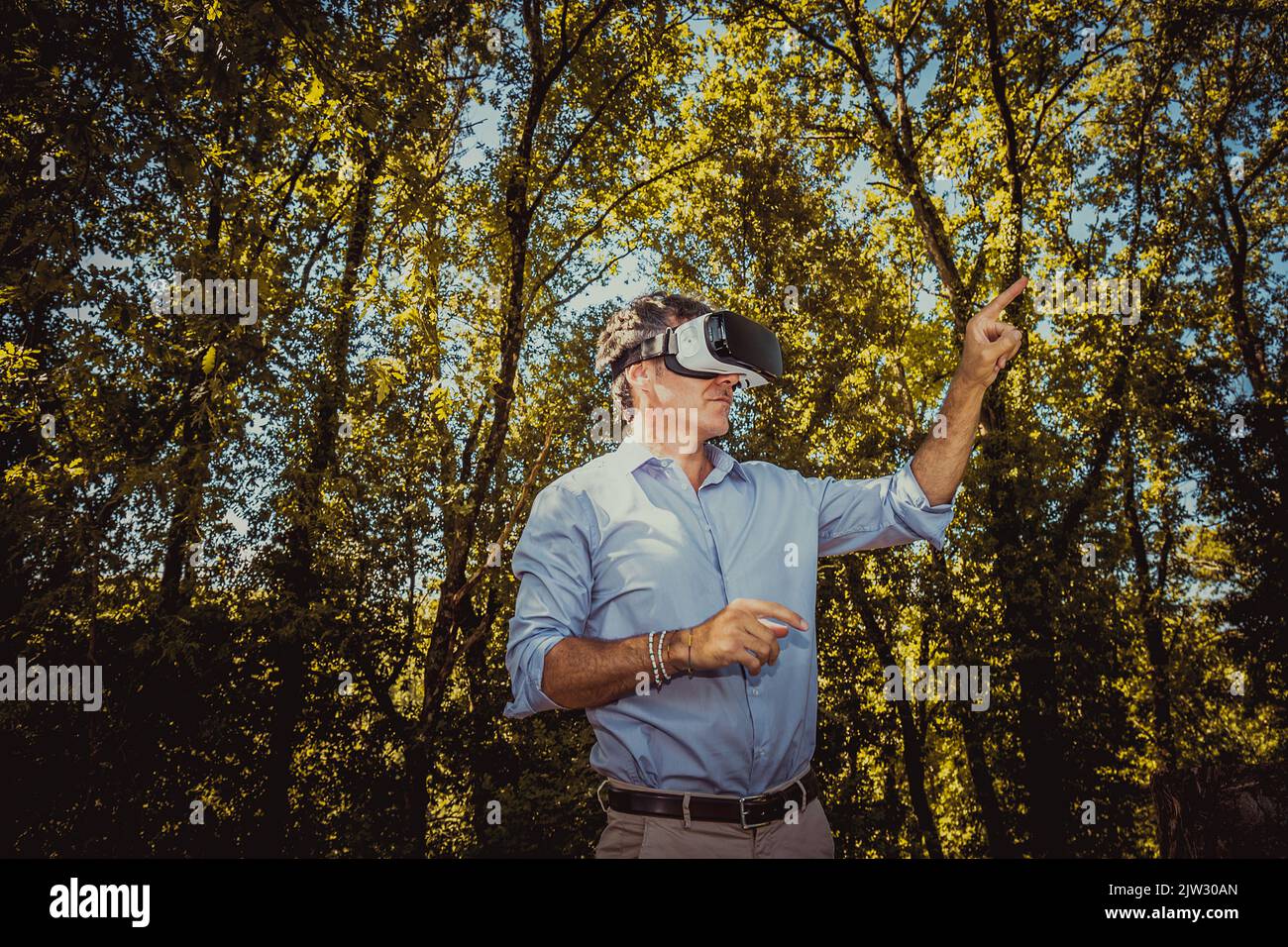 The young man is using a virtual reality viewer in the park. The handsome businessman is working with a virtual reality viewer outdoors. Stock Photo