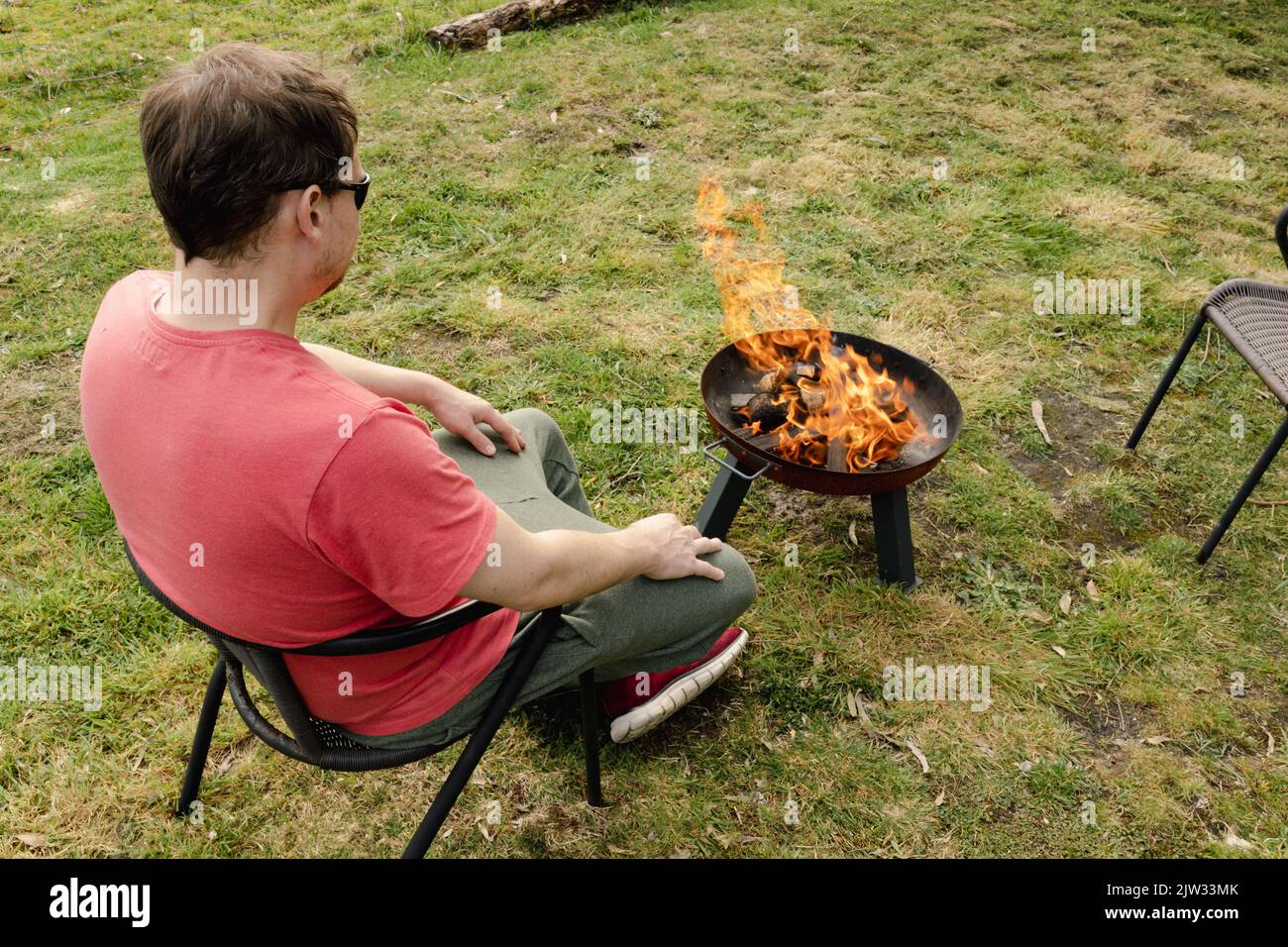 A man sitting by a lit fire next to a paddock in Australia Stock Photo