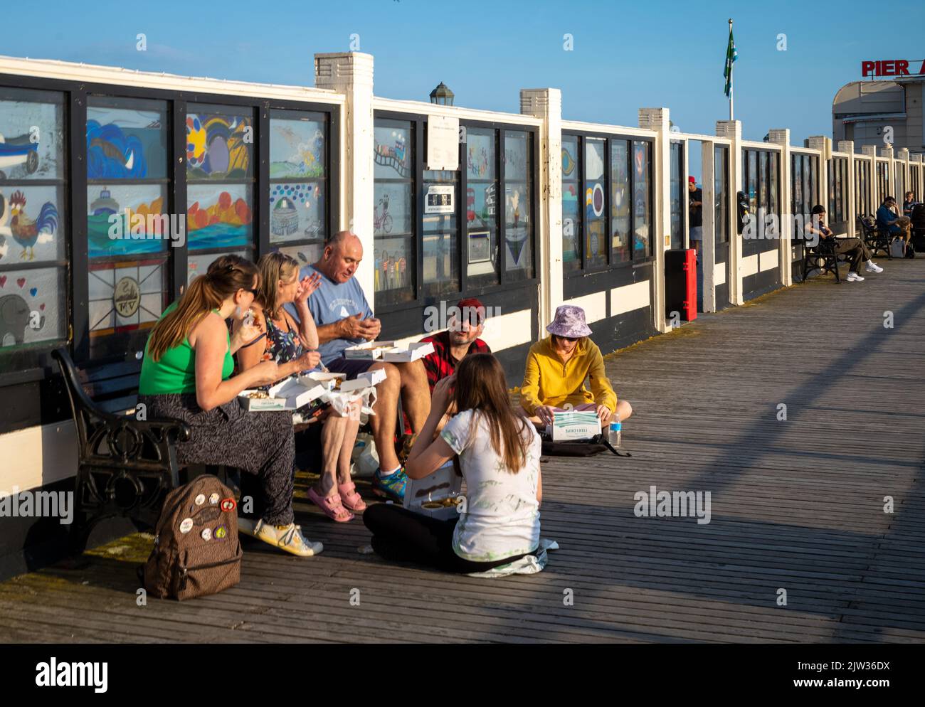 A family group sits to eat traditional fish and chips at the seaside on Worthing Pier, West Sussex, UK. Stock Photo