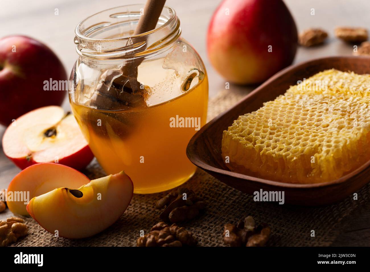 Mason jar with honey, honey dipper, honeycomb, red apples and walnuts on kitchen table Stock Photo