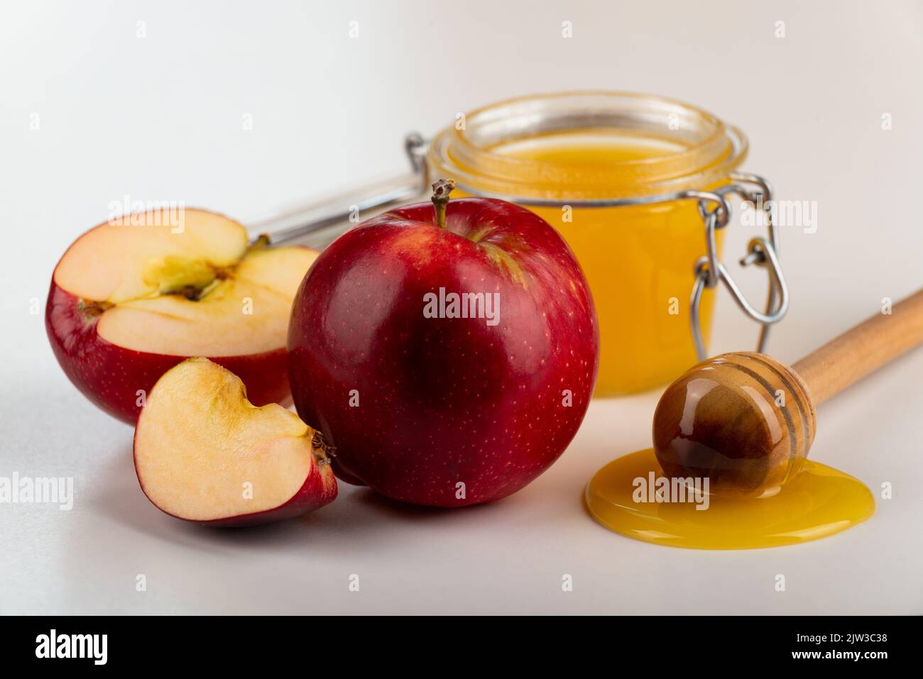 Mason jar with honey honey dipper and red apples on kitchen table Stock Photo