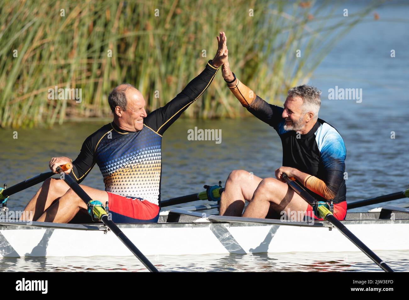 Two senior caucasian male rowers high fiving each other while rowing