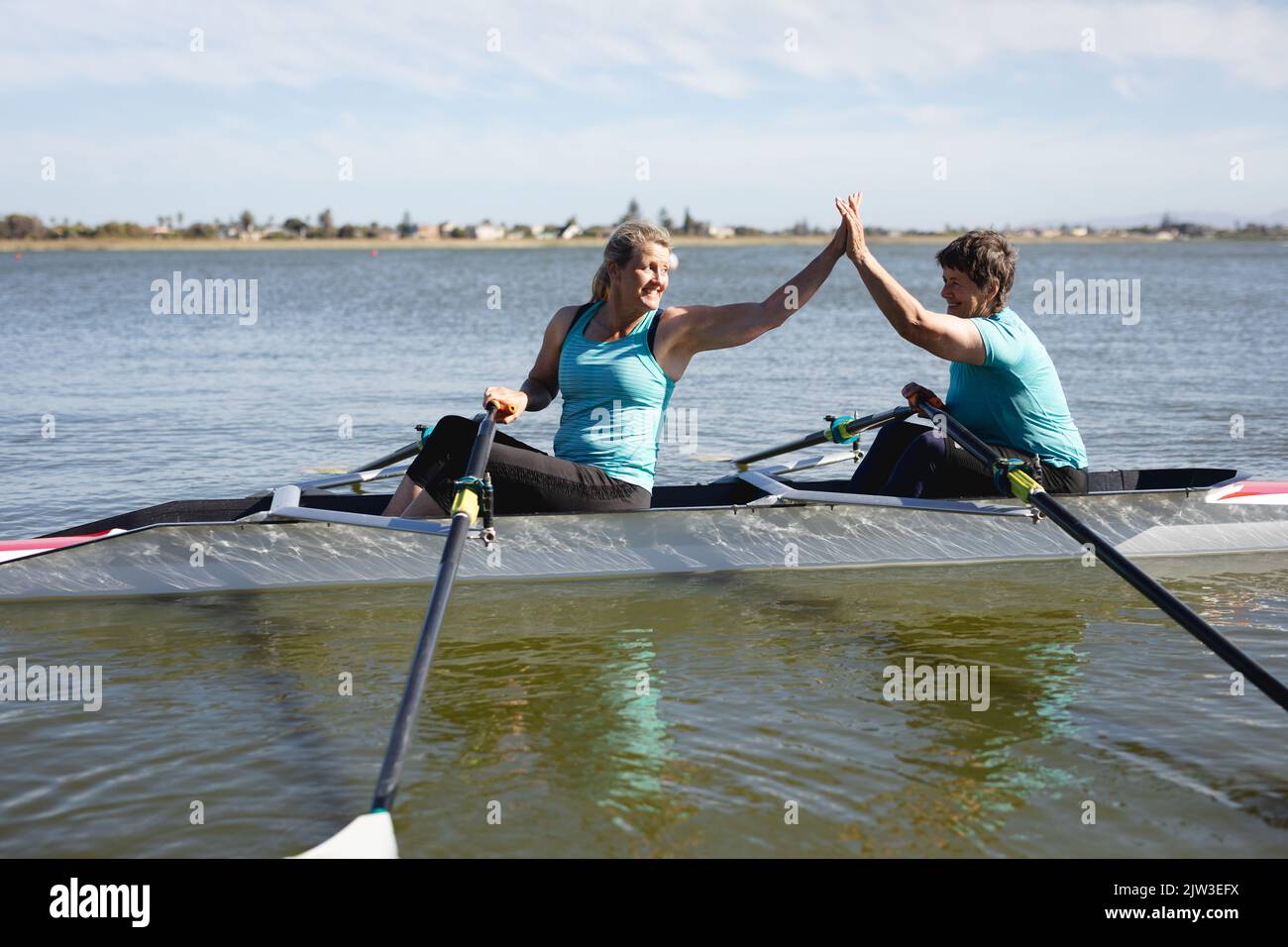Two senior caucasian female rowers high fiving each other while rowing