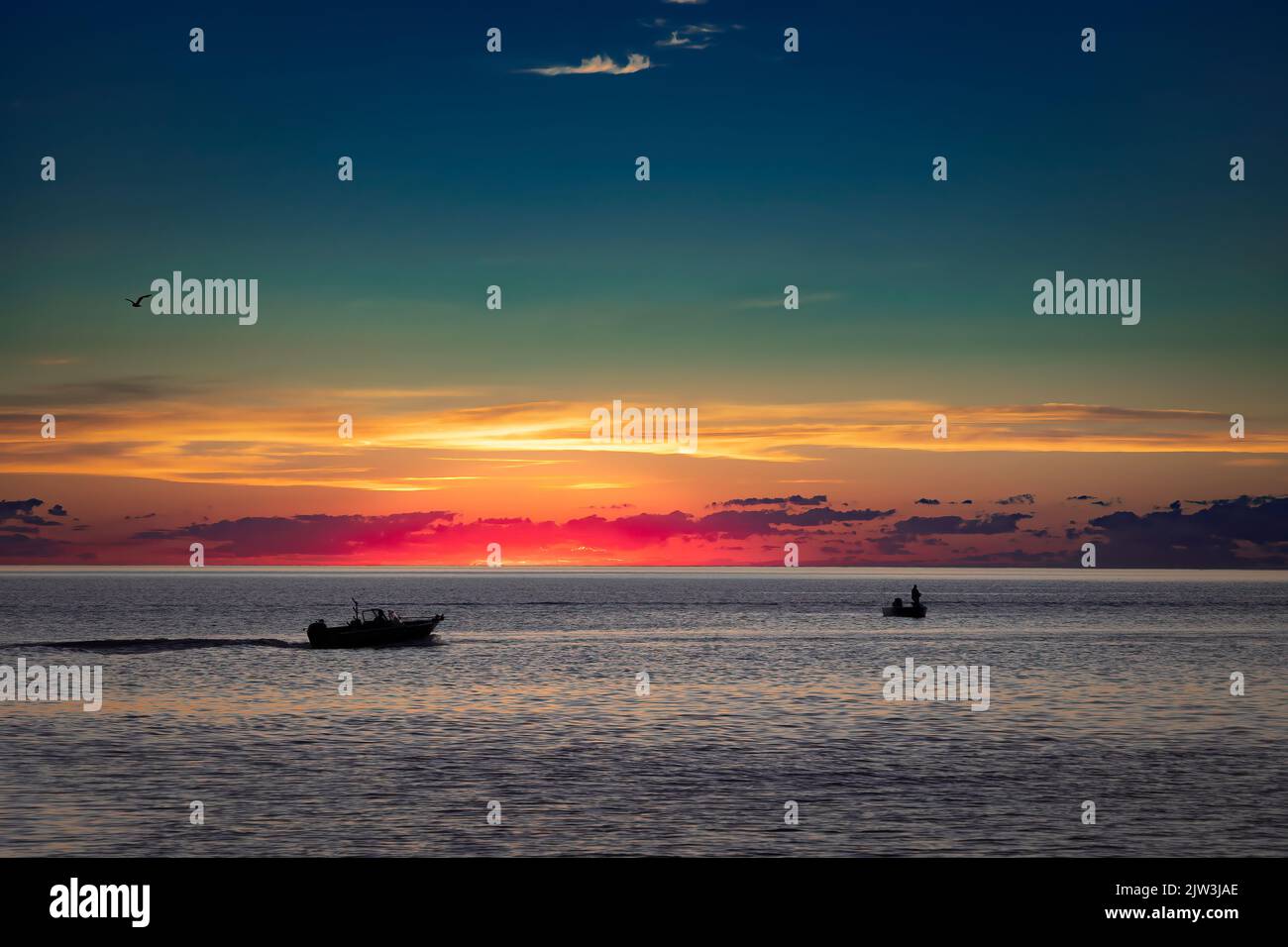 The morning sun is about to rise behind fishermen in their boats on Lake Michigan off the coast of Manitowoc, Wisconsin. Stock Photo