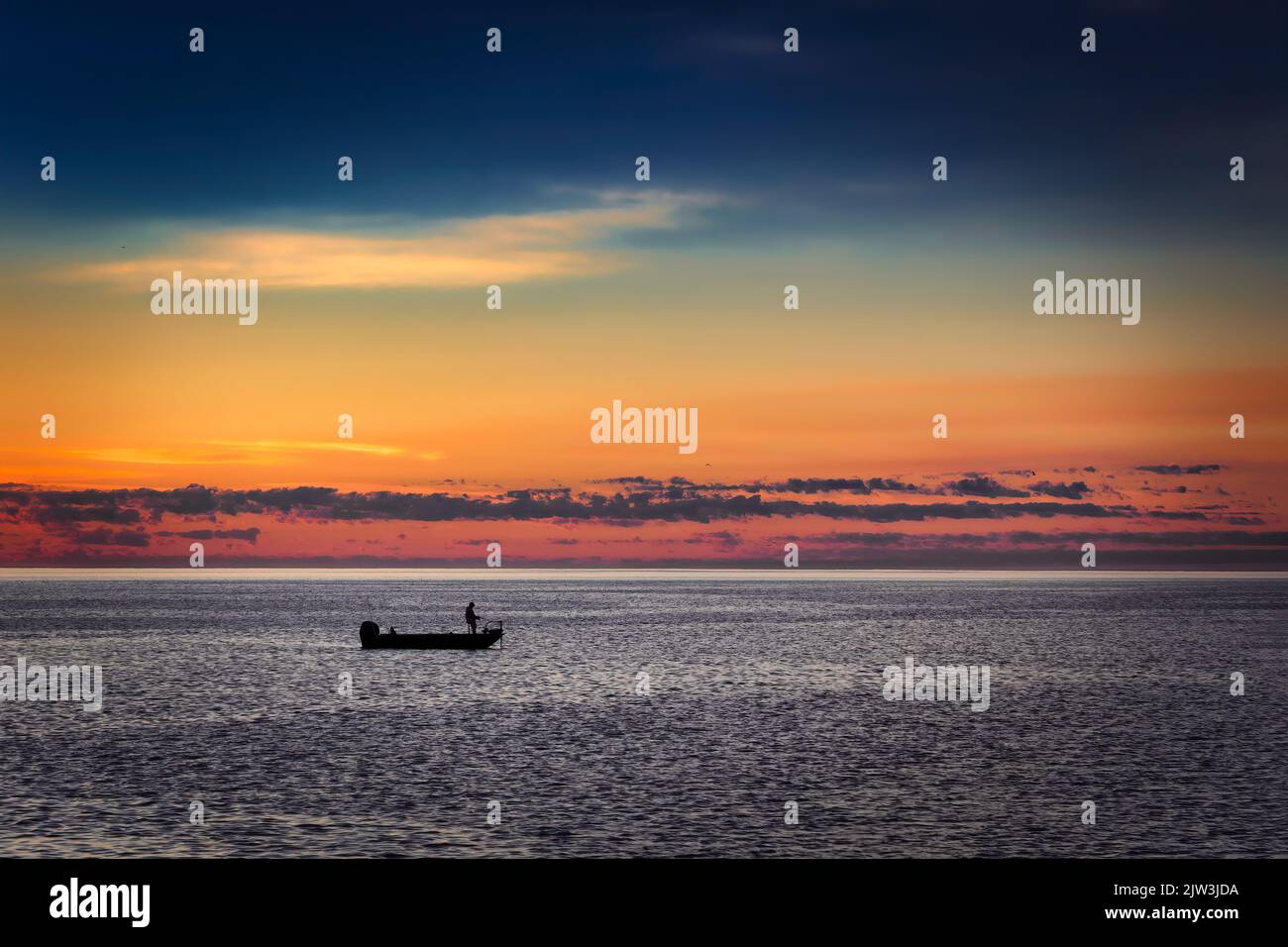 The morning sun is about to rise behind a fisherman in his boat on Lake Michigan off the coast of Manitowoc, Wisconsin. Stock Photo
