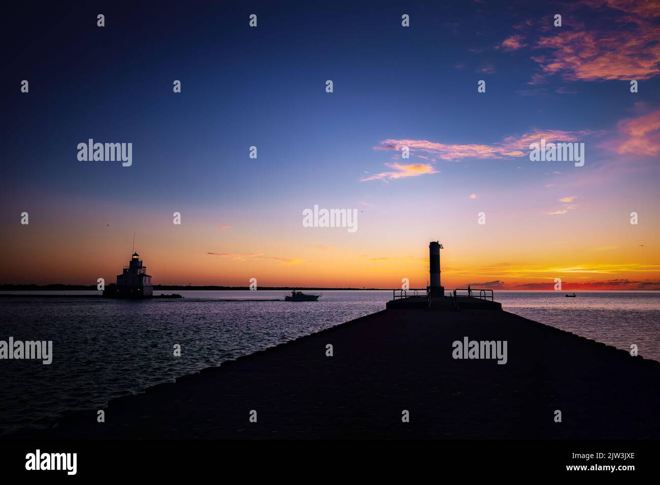 The silhouette of the south pier light at sunrise, with people fishing on Lake Michigan, at Manitowoc, Wisconsin. Stock Photo