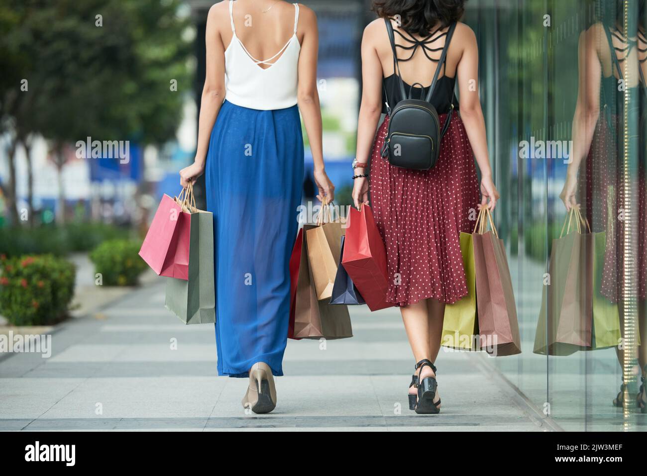 Rear view of young woman with shopping bags walking along the street ...