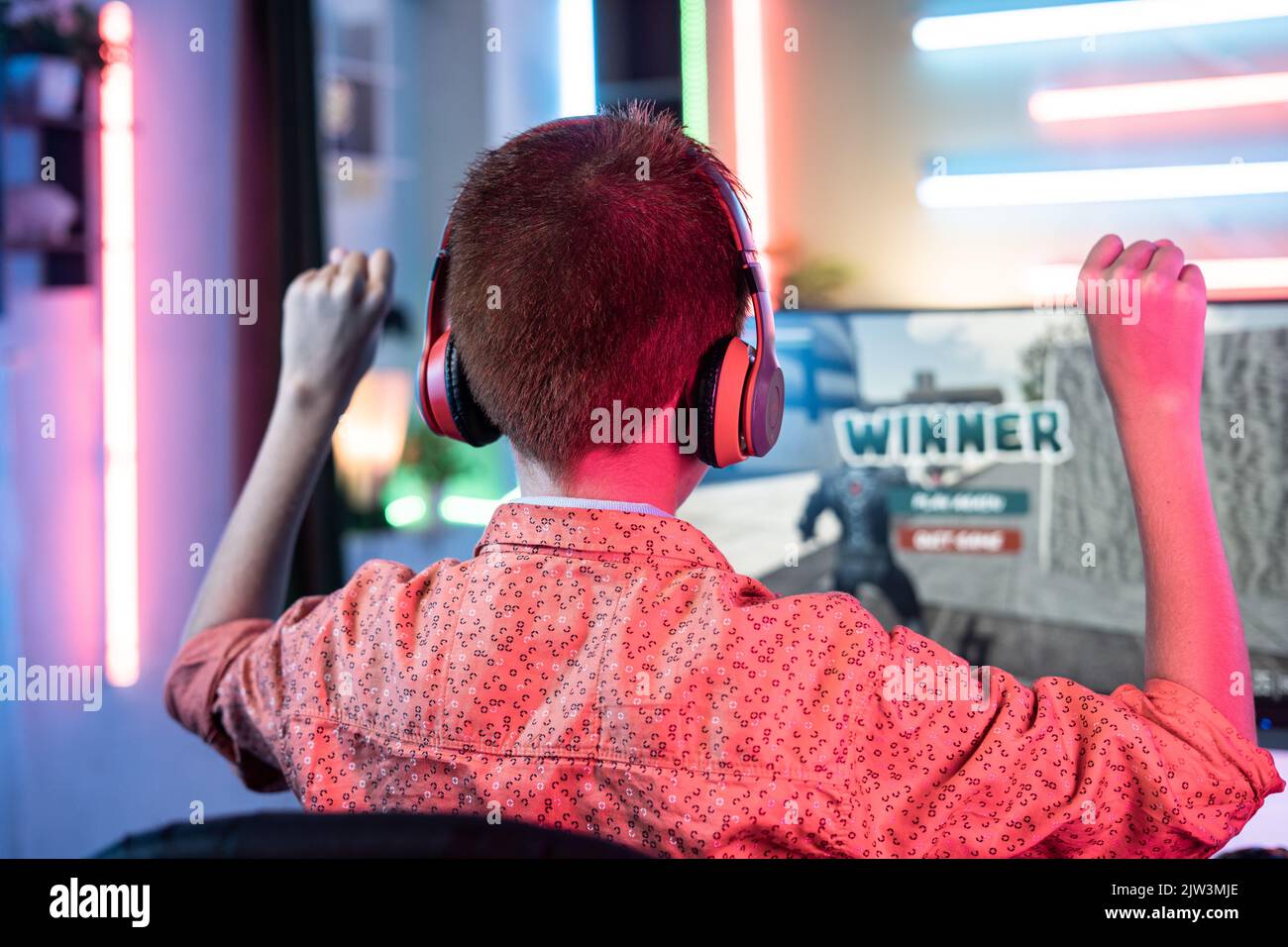 Back view shot of teenager kid celebrating victory by dancing on chair while playing video game on computer at home - concept of achievement, positive Stock Photo