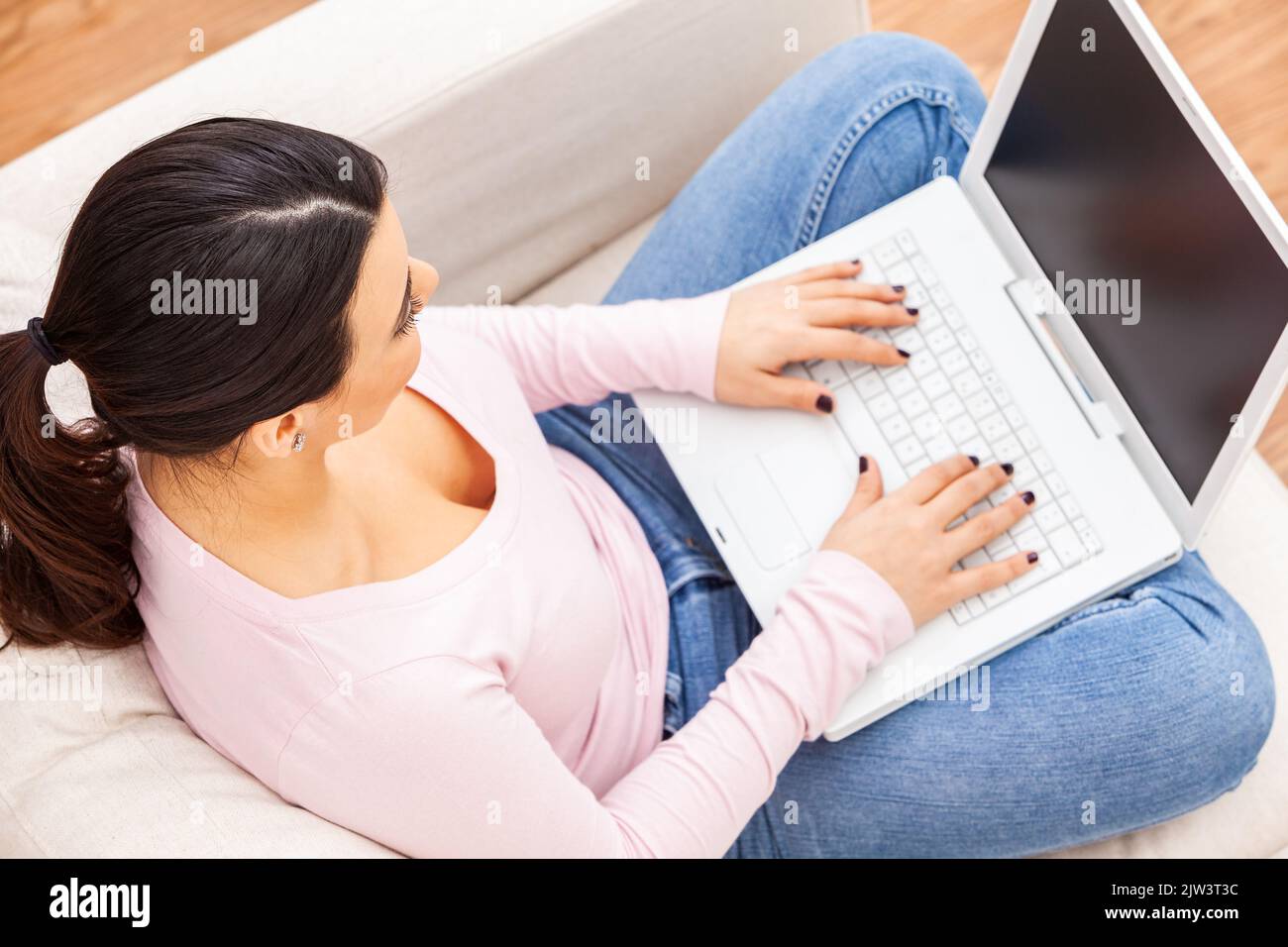 Beautiful  Latina Hispanic girl female young woman using a laptop computer for on line shopping, social media or working at home on her sofa Stock Photo