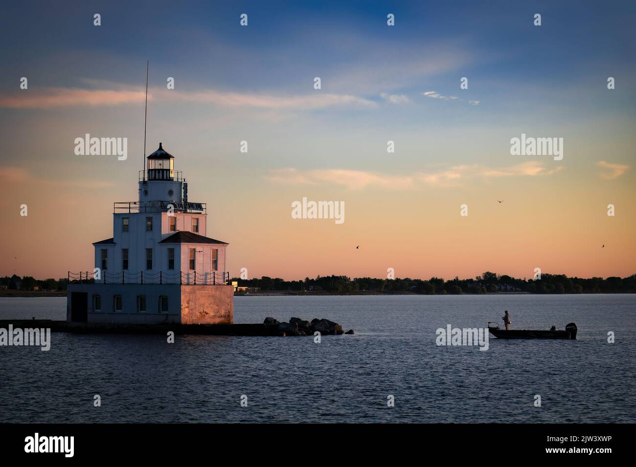A fisherman in his boat casts his line by the Lake Michigan lighthouse at Manitowoc, Wisconsin. Stock Photo