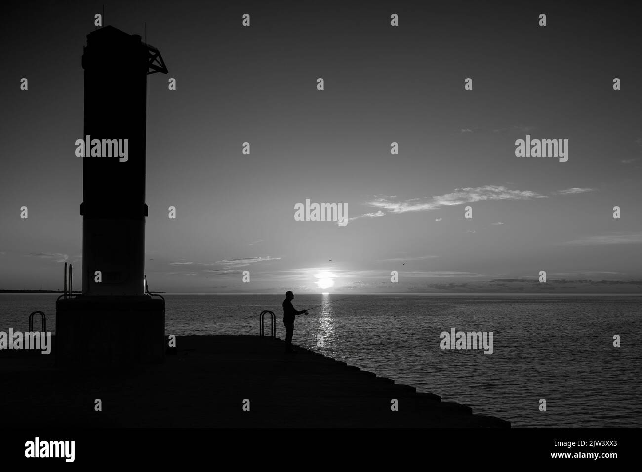 The silhouette of a man fishing at sunrise from the south pier on Lake Michigan at Manitowoc, Wisconsin. Stock Photo