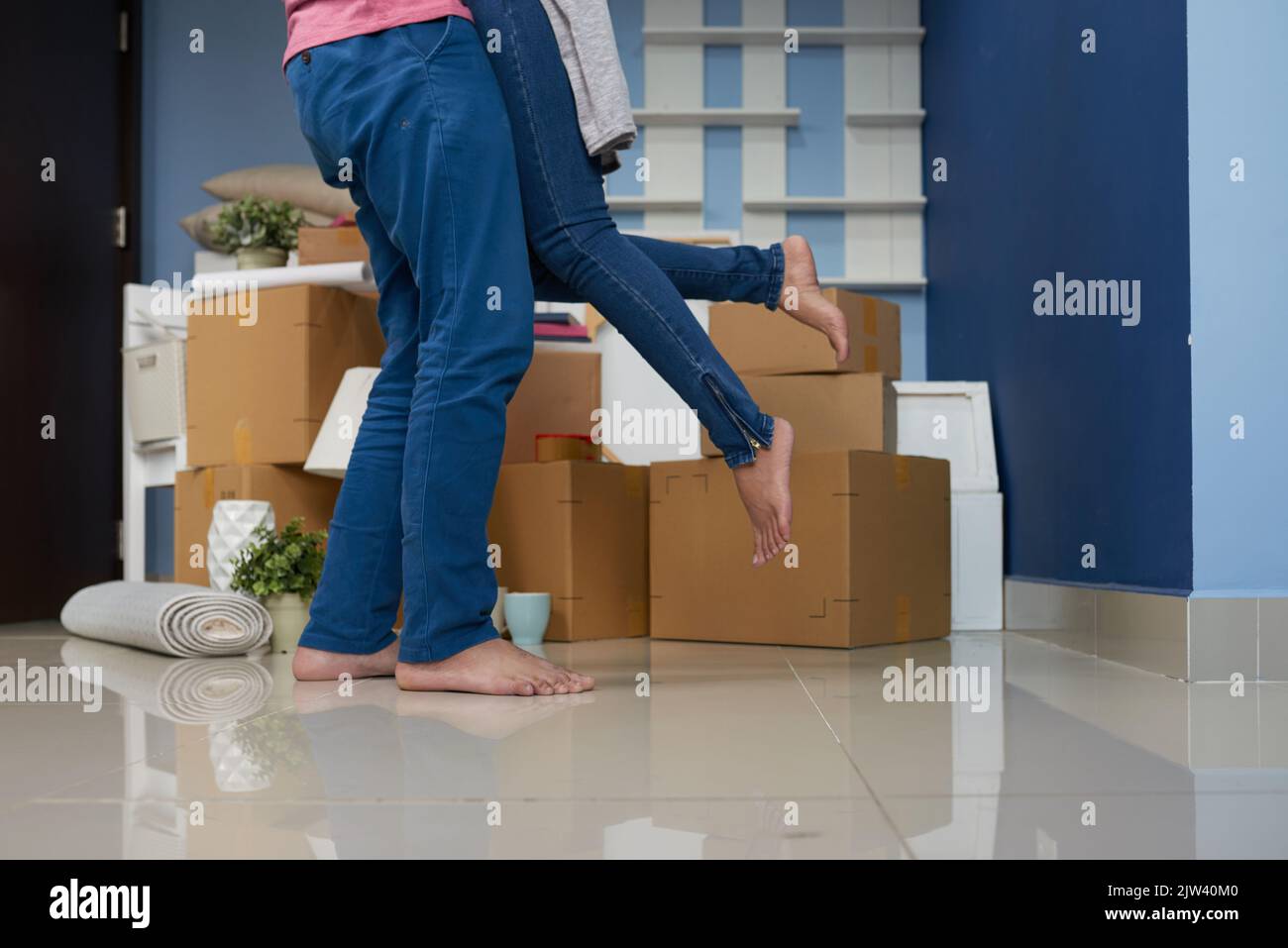Unrecognizable man lifting his beloved while standing in new apartment with packed cardboard boxes Stock Photo