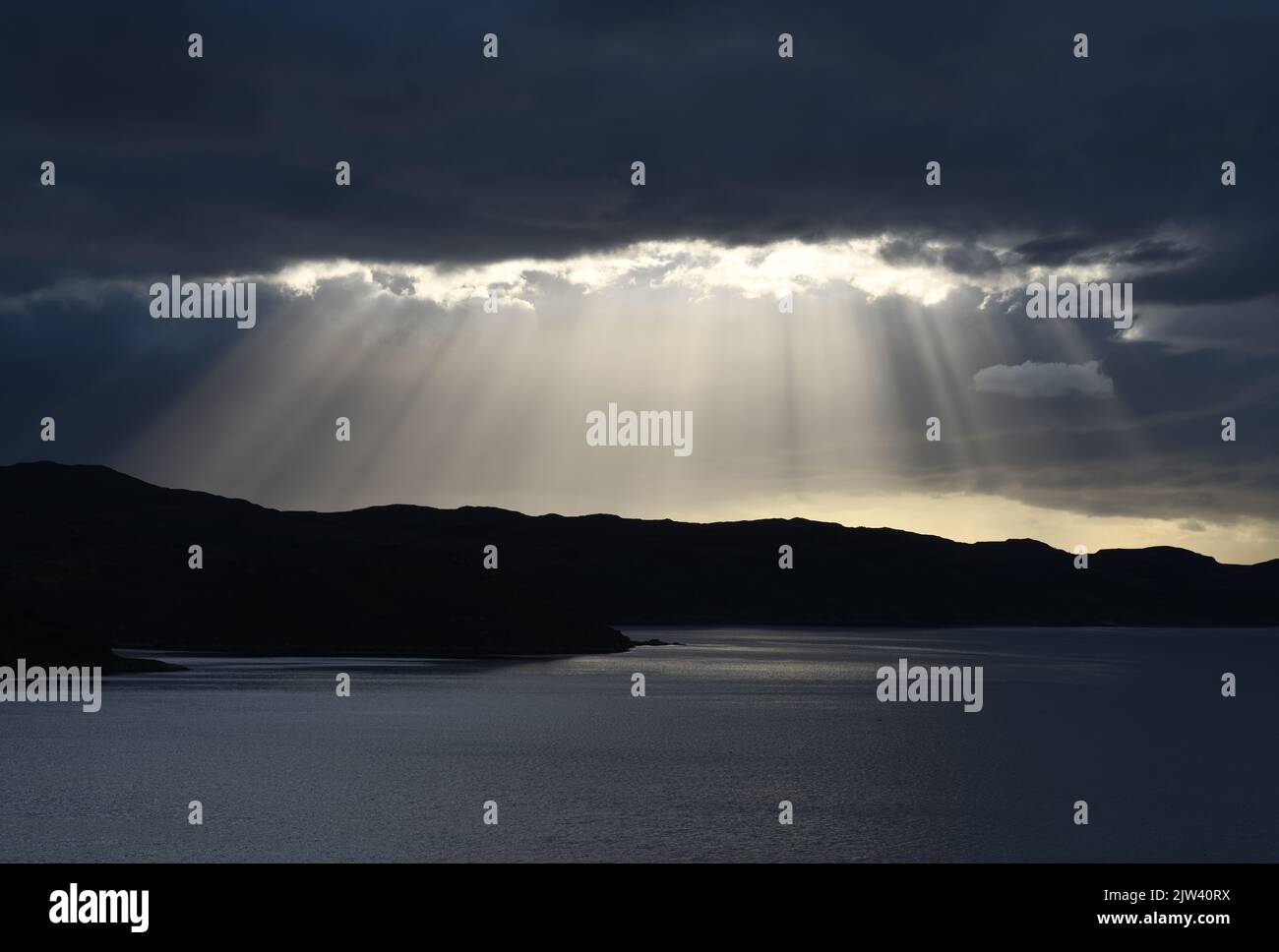 Heavy clouds split to allow the suns rays to create a stunning sunset over the north west coast of Scotland at Kylesku on the North coast 500. Stock Photo