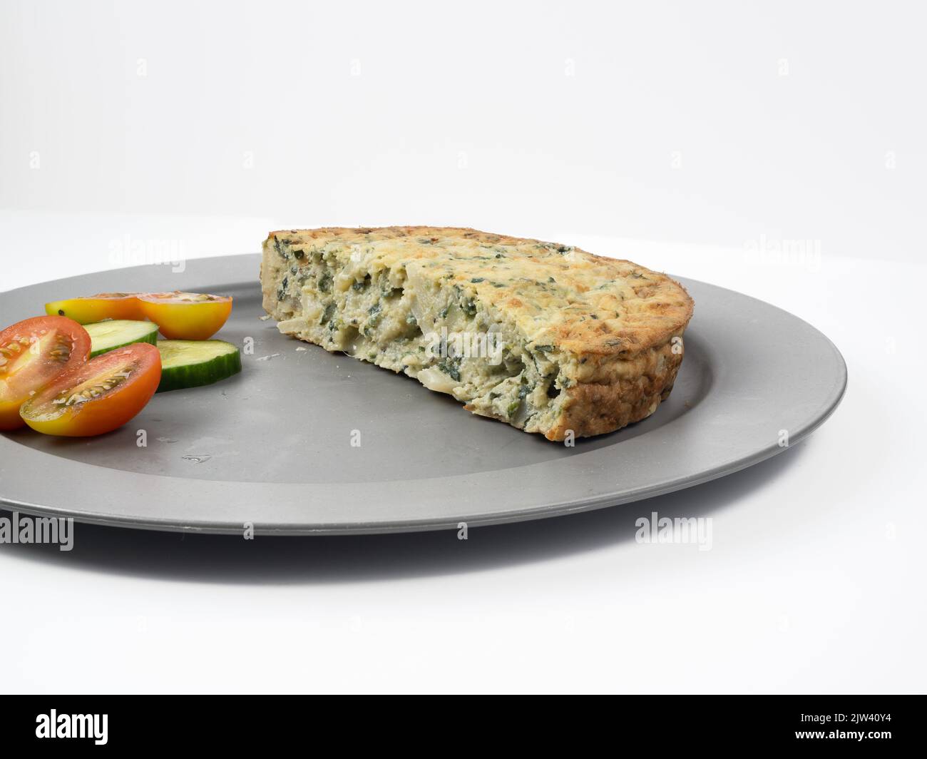 portion of freshly baked spinach and cheddar Frittata with a side salad on a white background Stock Photo