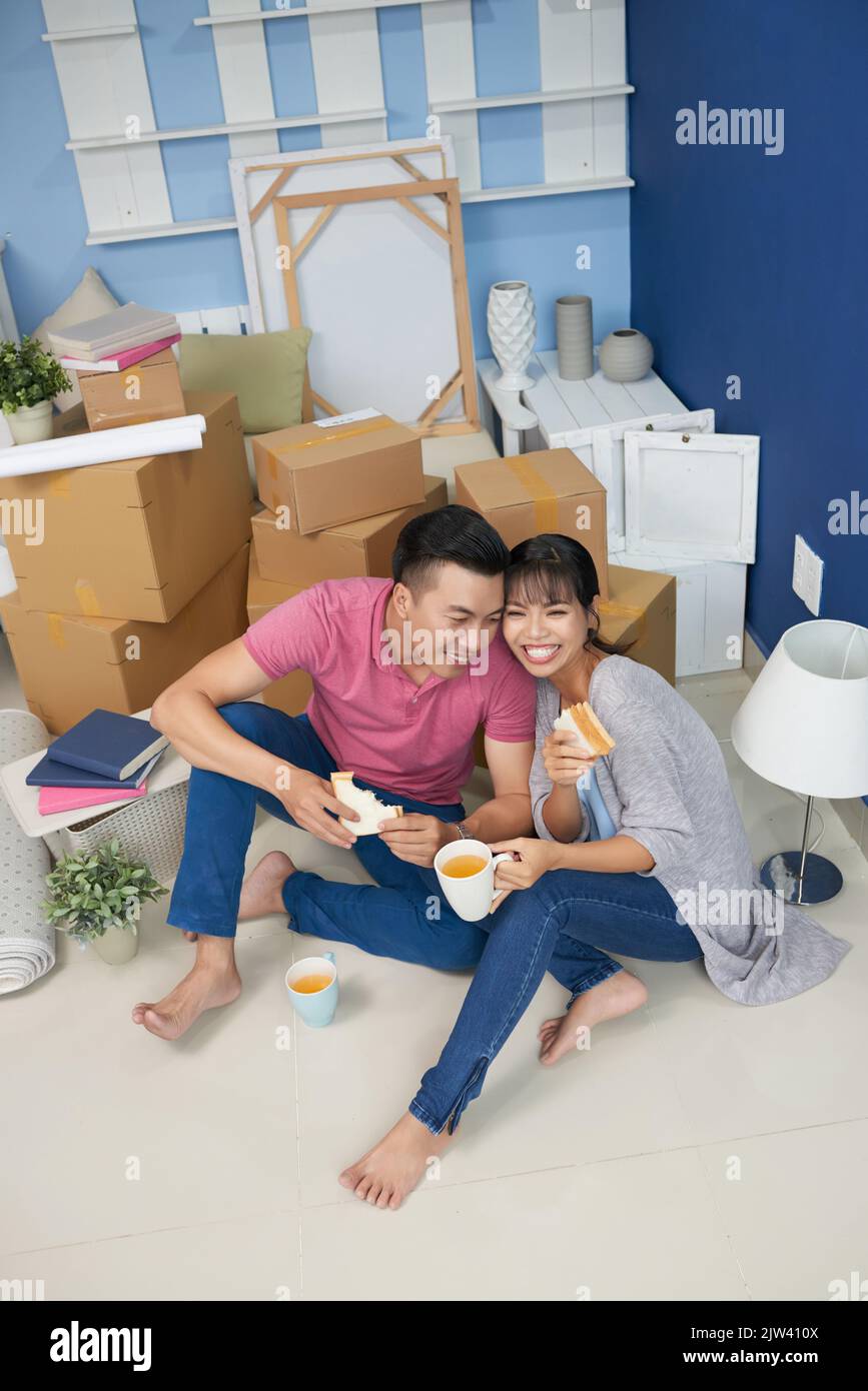 Young Asian couple eating sandwiches and smiling happily while sitting
