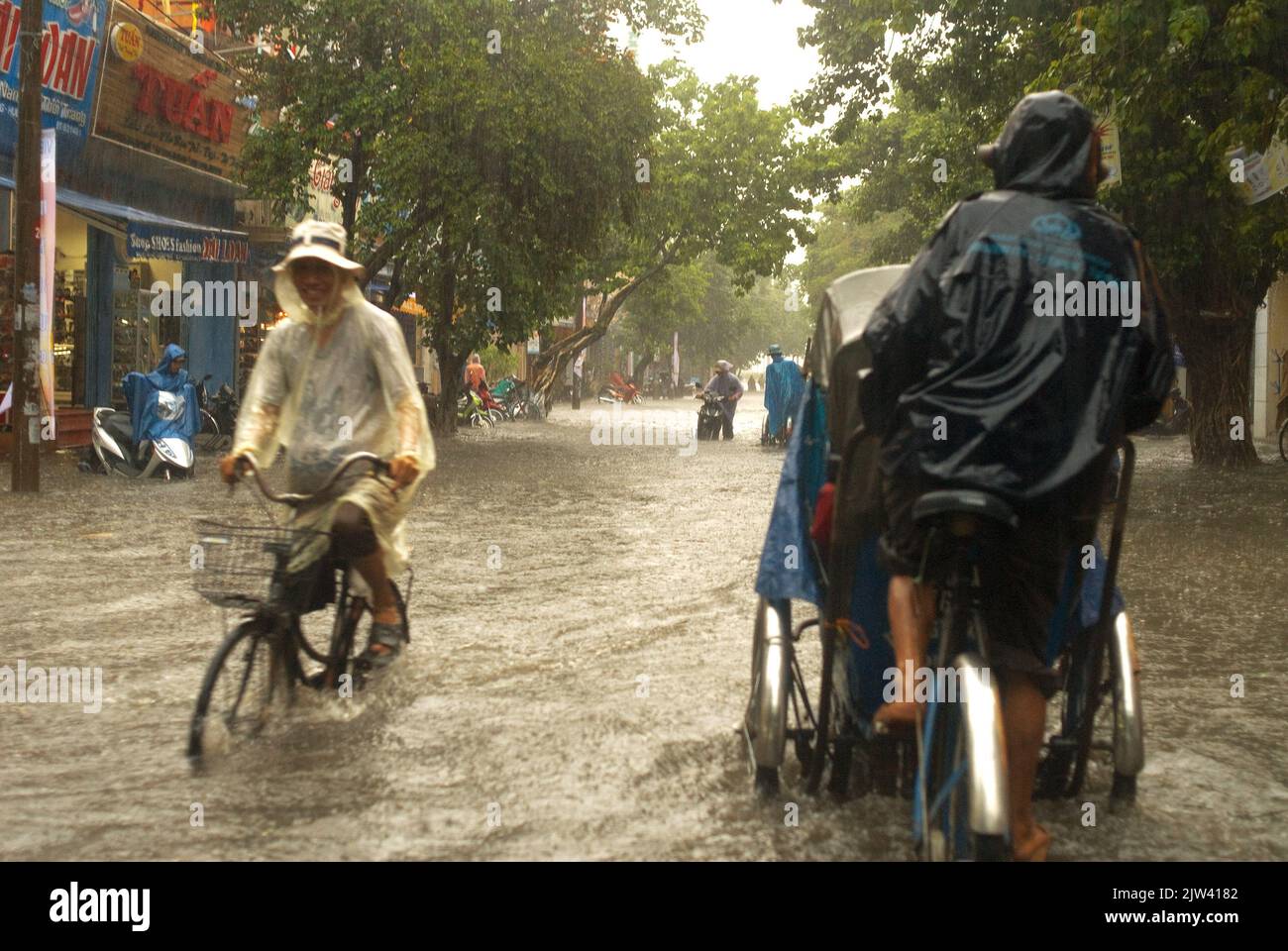 Monsoon rains in the city of Hue. People in tuc-tuc rides bicycle along flooded streets in Hue. Vietnam.   floods. Much of India is facing increasingl Stock Photo