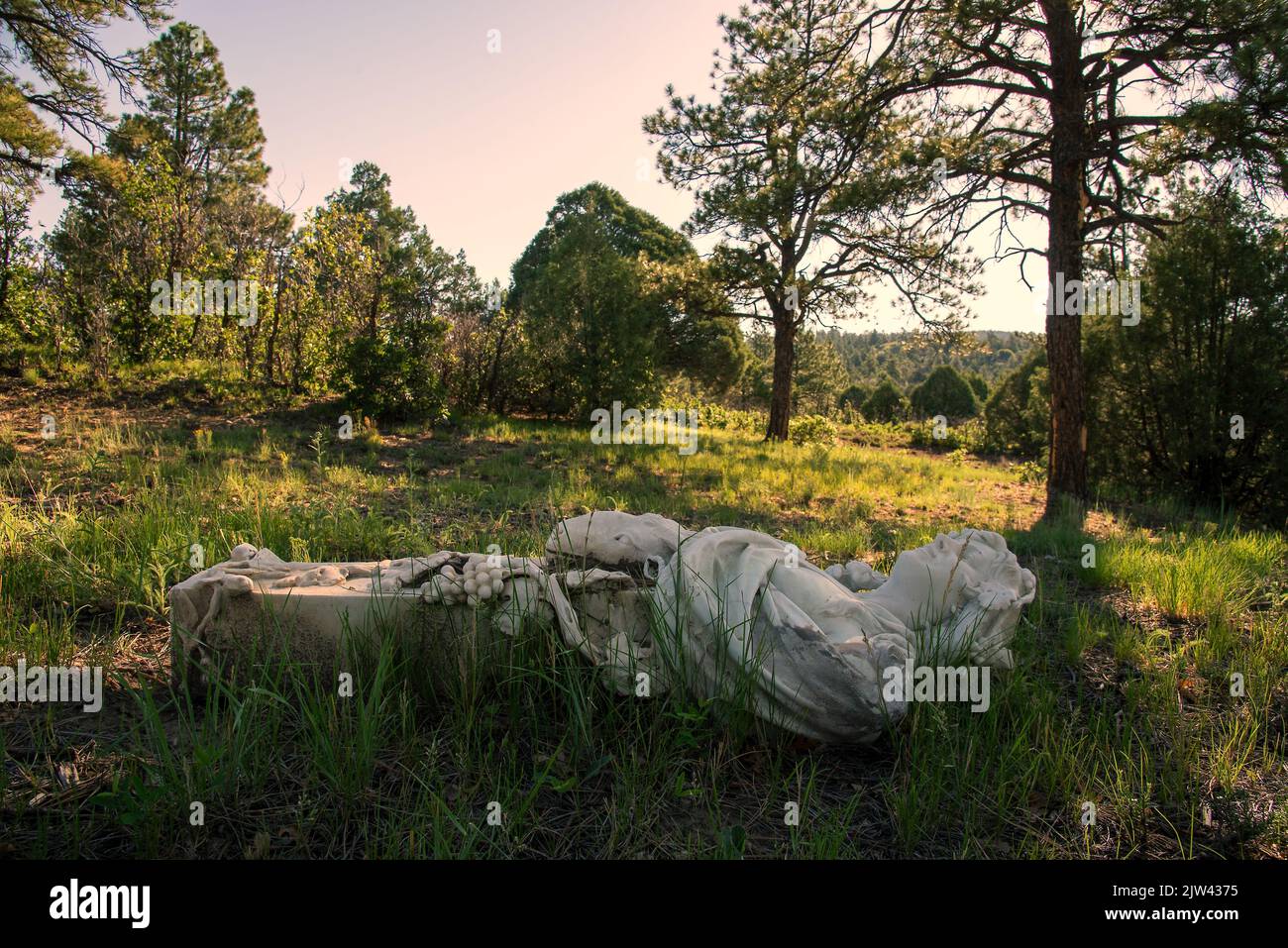 A fallen marble statue of a woman holding foods that represent harvest, lying on it’s back. Stock Photo