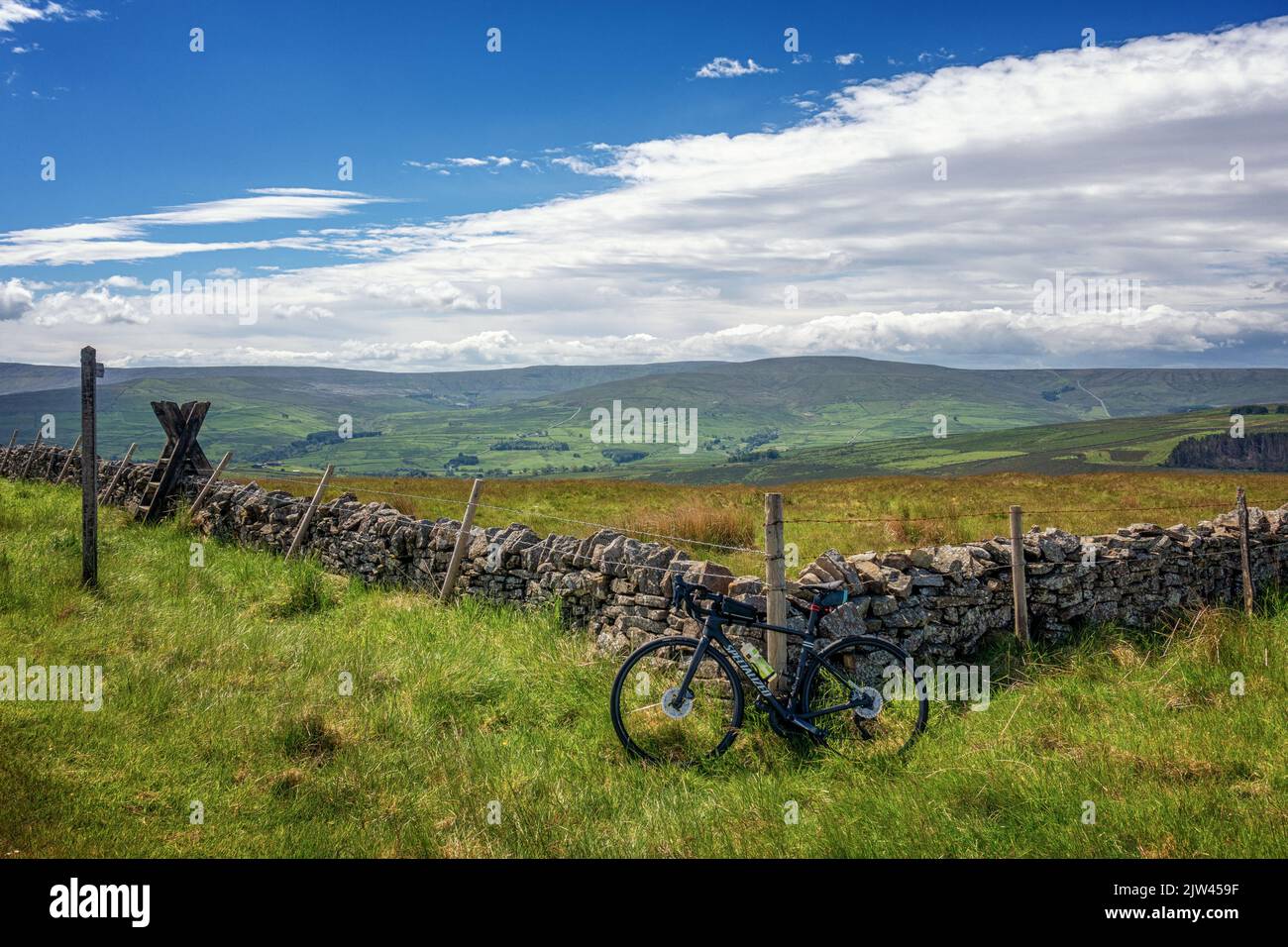 Views looking into the Weardale Valley and across to Cross Fell from the top of Peat Hill cycling climb with a road bike leaning against an old stone Stock Photo