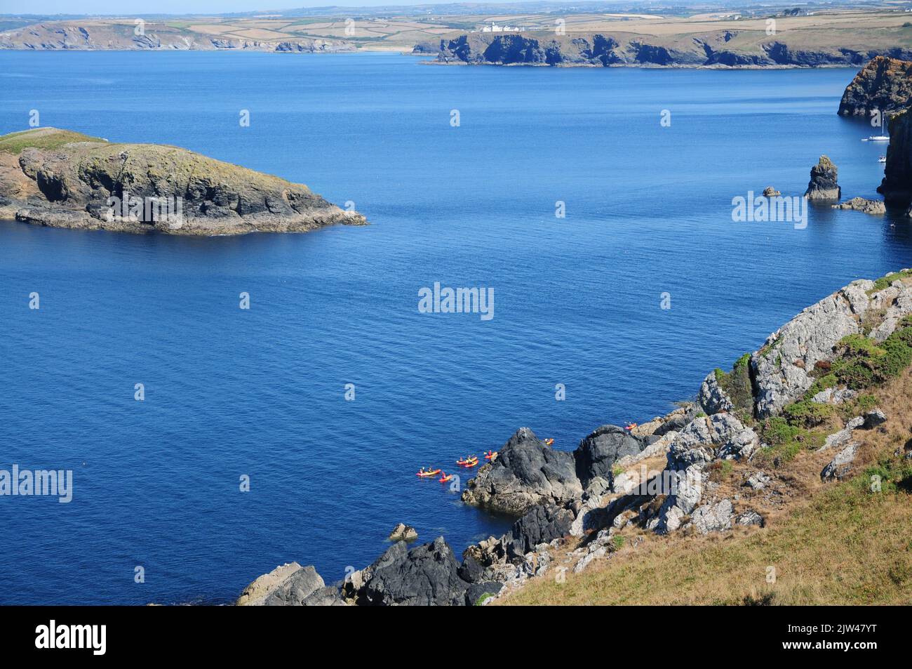 Kayakers explore the rocky coastline on a calm day near Mullion Cove, Cornwall Stock Photo