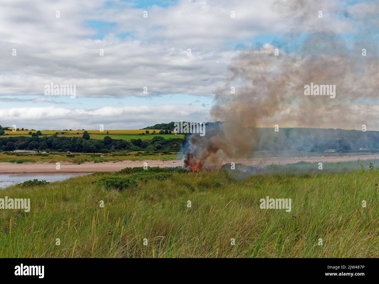 Flames and smoke from a Wildfire in the Gorse and Grasses behind the Dunes of Montrose Beach, with the River North Esk in the background. Stock Photo