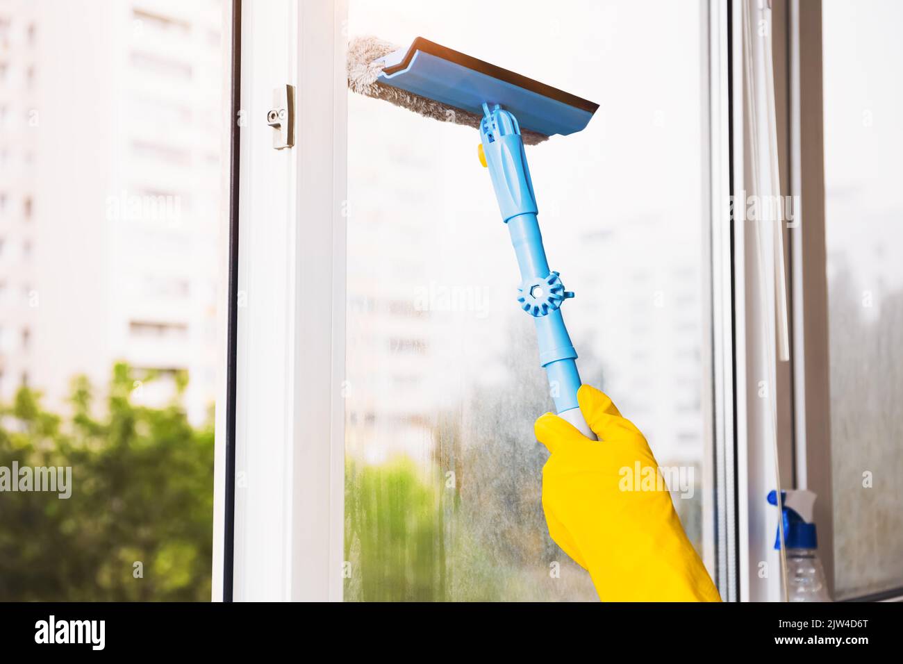 Man in yellow gloves cleaning window with squeegee and spray detergent