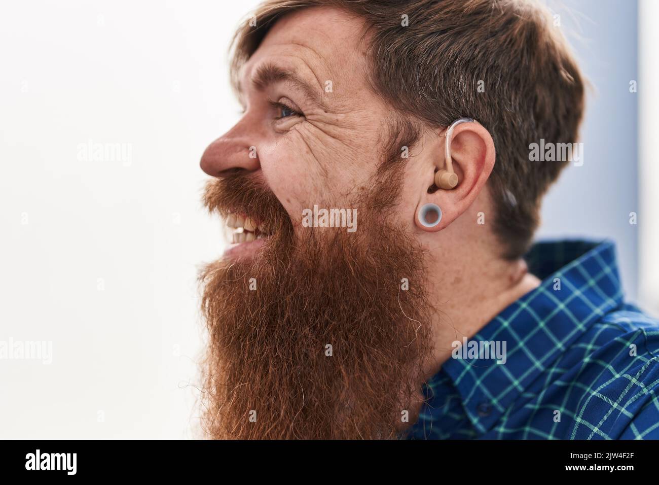 Young redhead man using deafness aid machine sitting on sofa at home Stock Photo