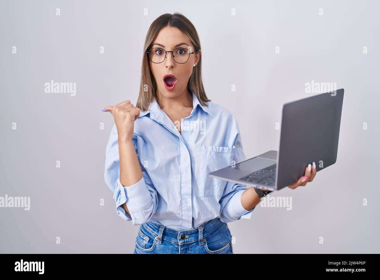 Young woman working using computer laptop surprised pointing with hand ...
