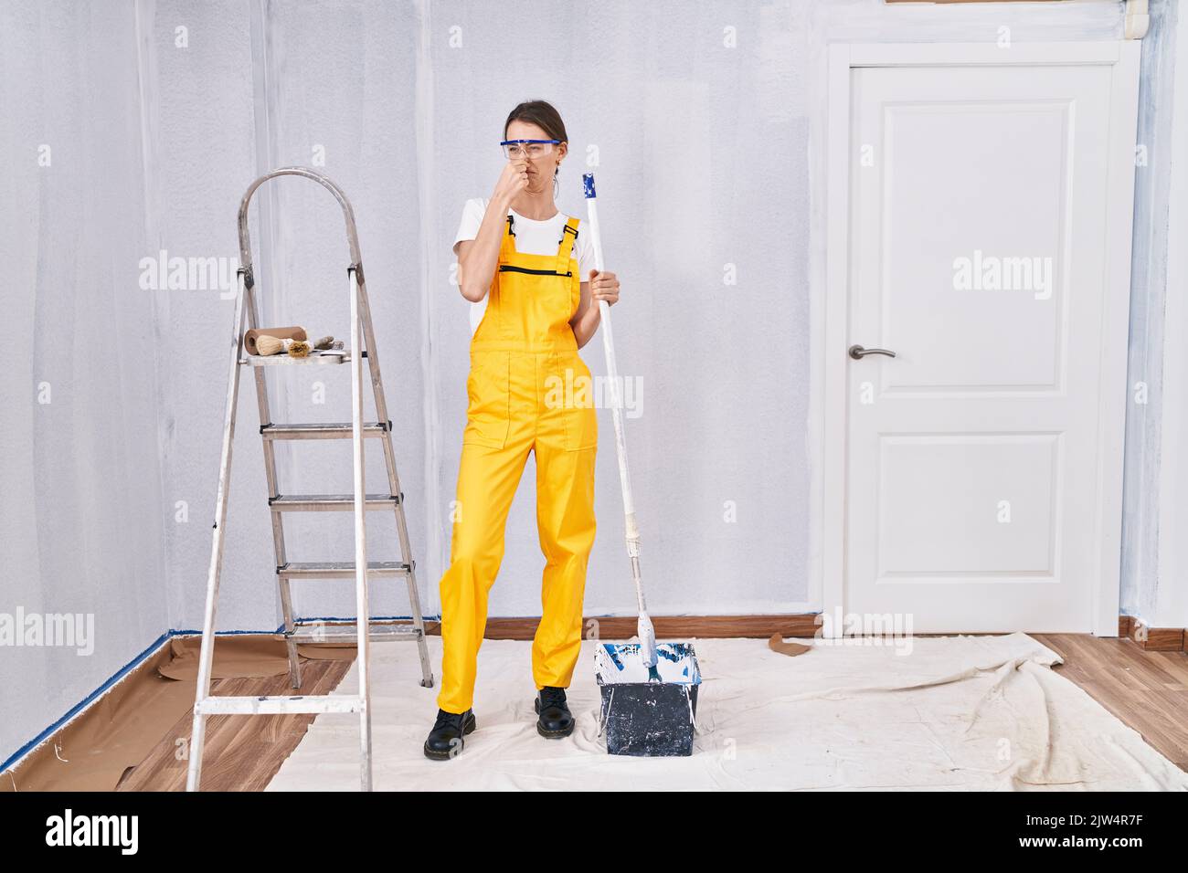 Young caucasian woman painting walls smelling something stinky and