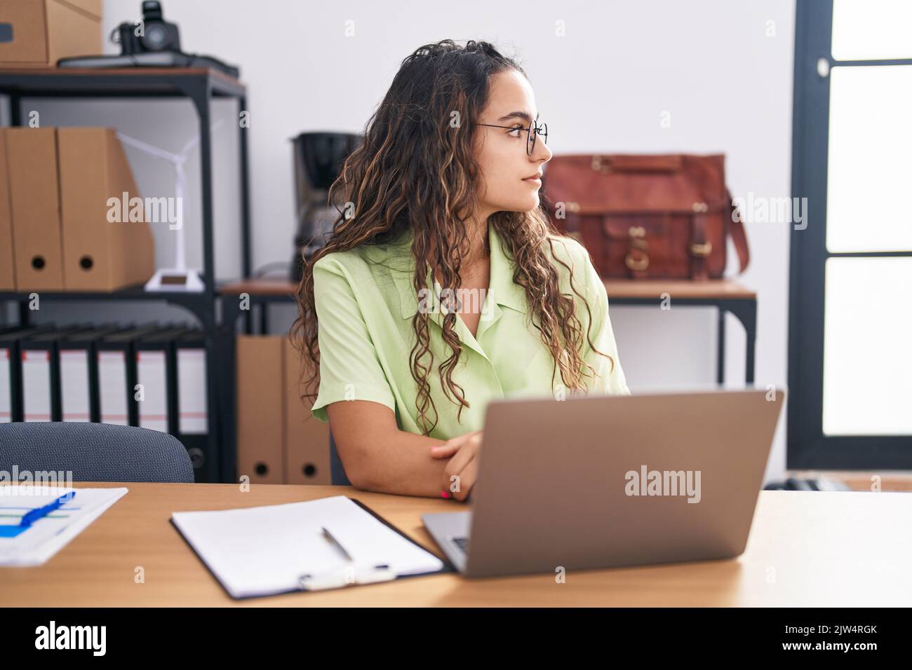Young hispanic woman working at the office wearing glasses looking to ...