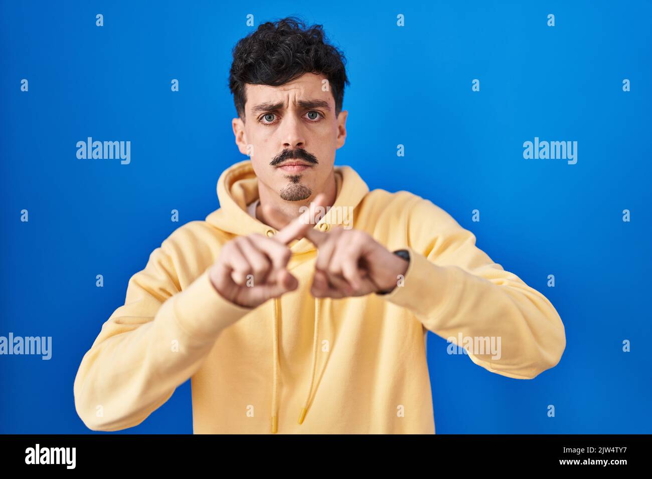 Hispanic man standing over blue background rejection expression ...
