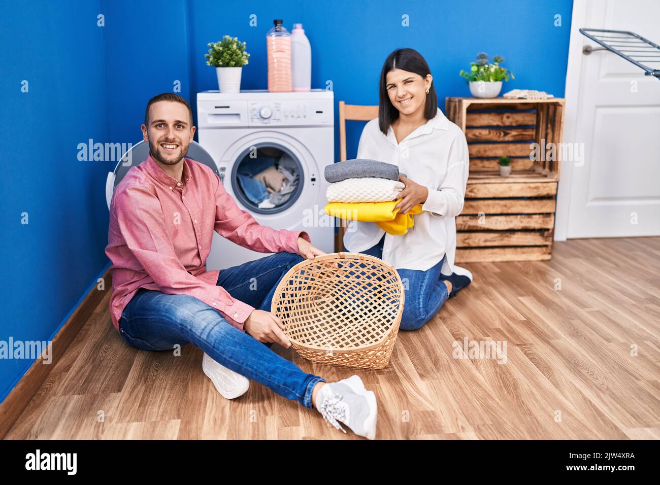 Young couple doing laundry at home smiling with a happy and cool smile ...