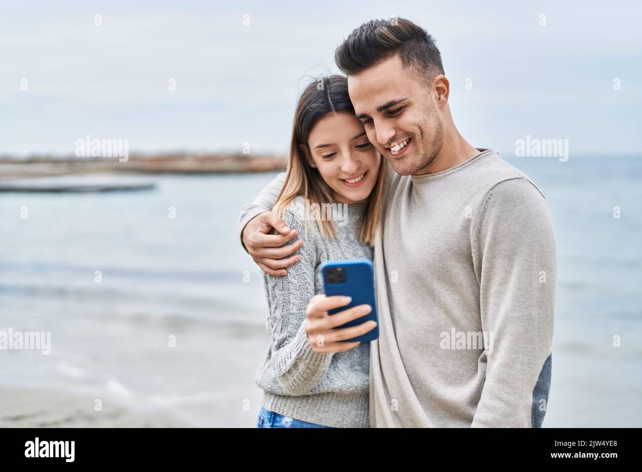 Man and woman couple hugging each other using smartphone at seaside ...