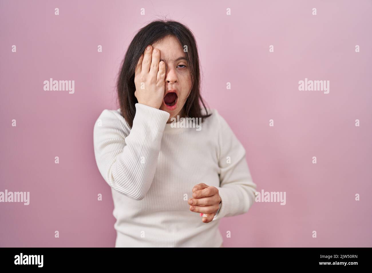 Woman with down syndrome standing over pink background yawning tired