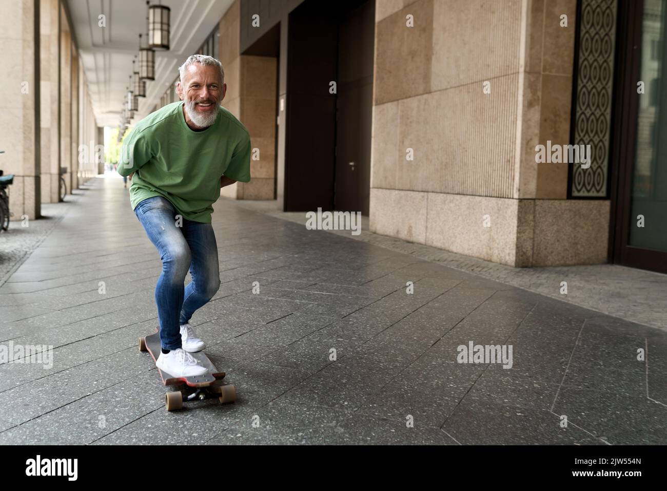 Active happy cool older man skater riding skateboard in the city street. Stock Photo