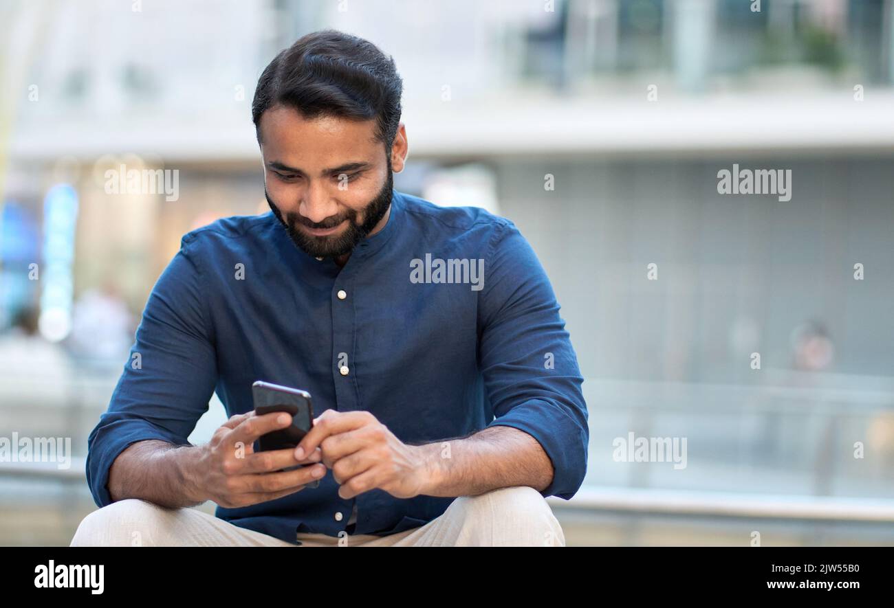 Indian business man using cell phone sitting on urban city street Stock