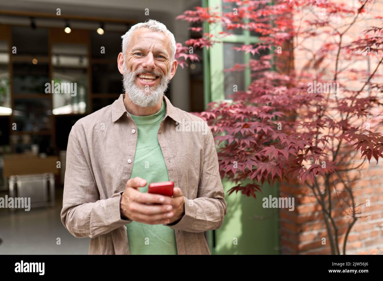 Smiling older middle aged man using phone standing outdoors. Stock Photo