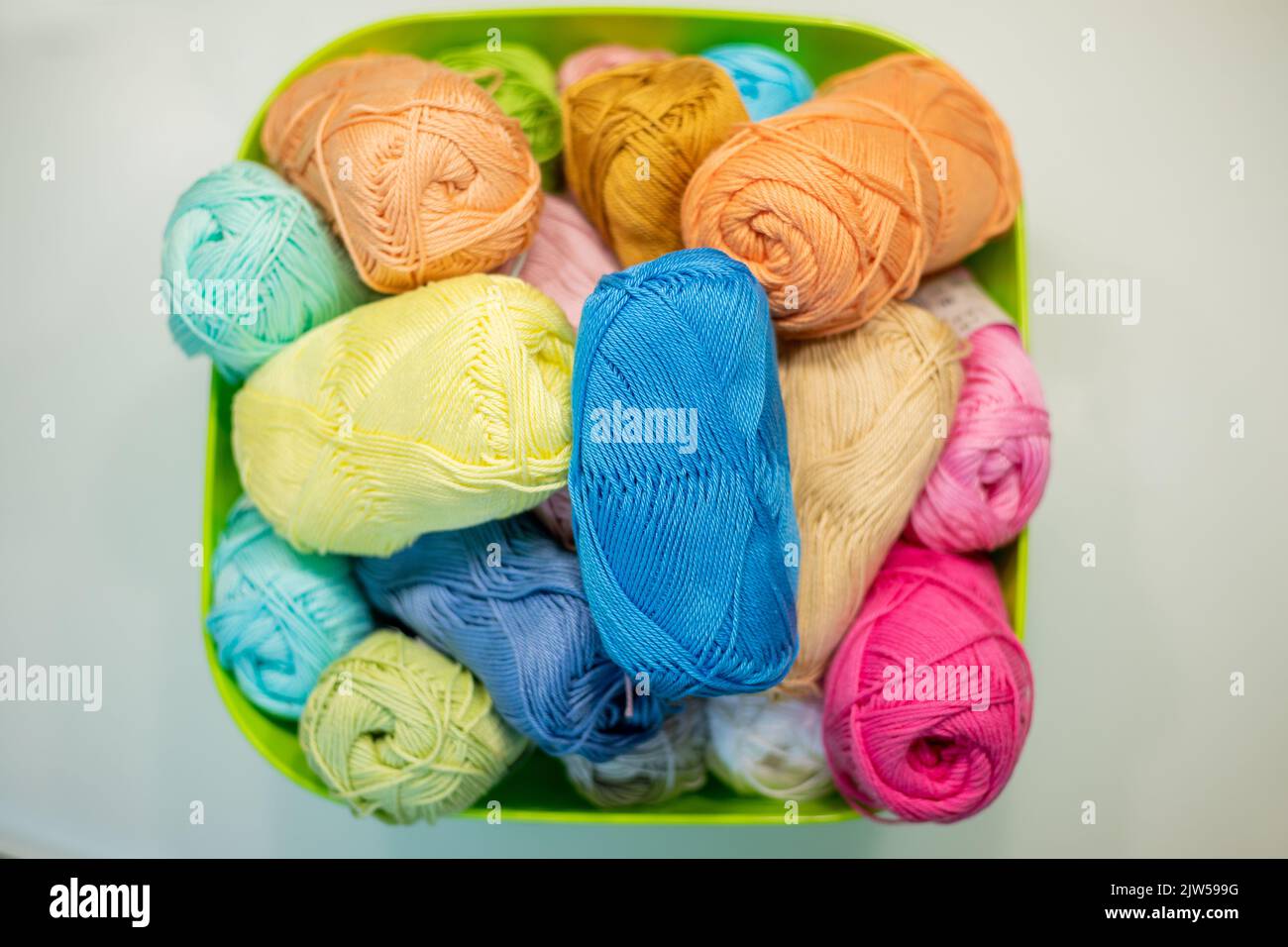 Multi-colored bright yarn lies in a box on a white table, selective focus. Stock Photo