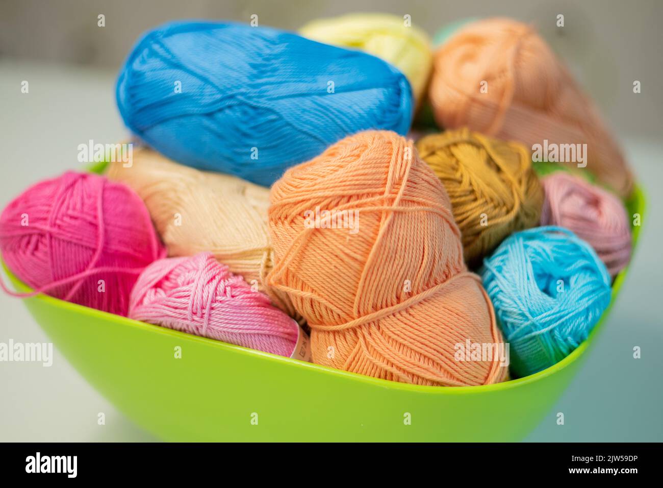 Multi-colored bright yarn lies in a box on a white table, selective focus. Stock Photo
