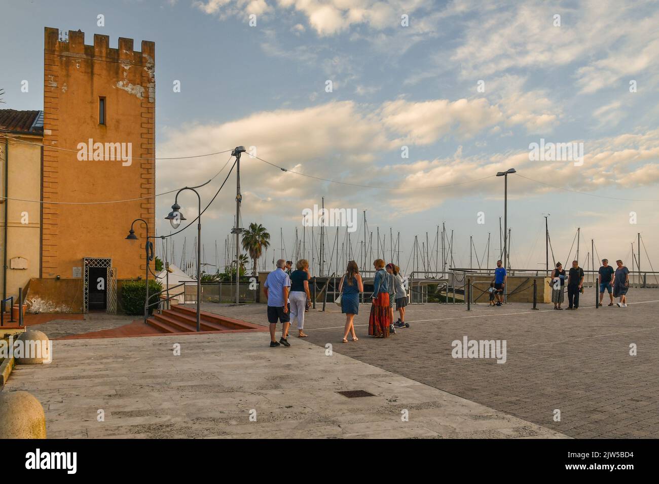 The waterfront of San Vincenzo with the medieval tower overlooking the harbor and tourists walking at sunset, Livorno, Tuscany, Italy Stock Photo