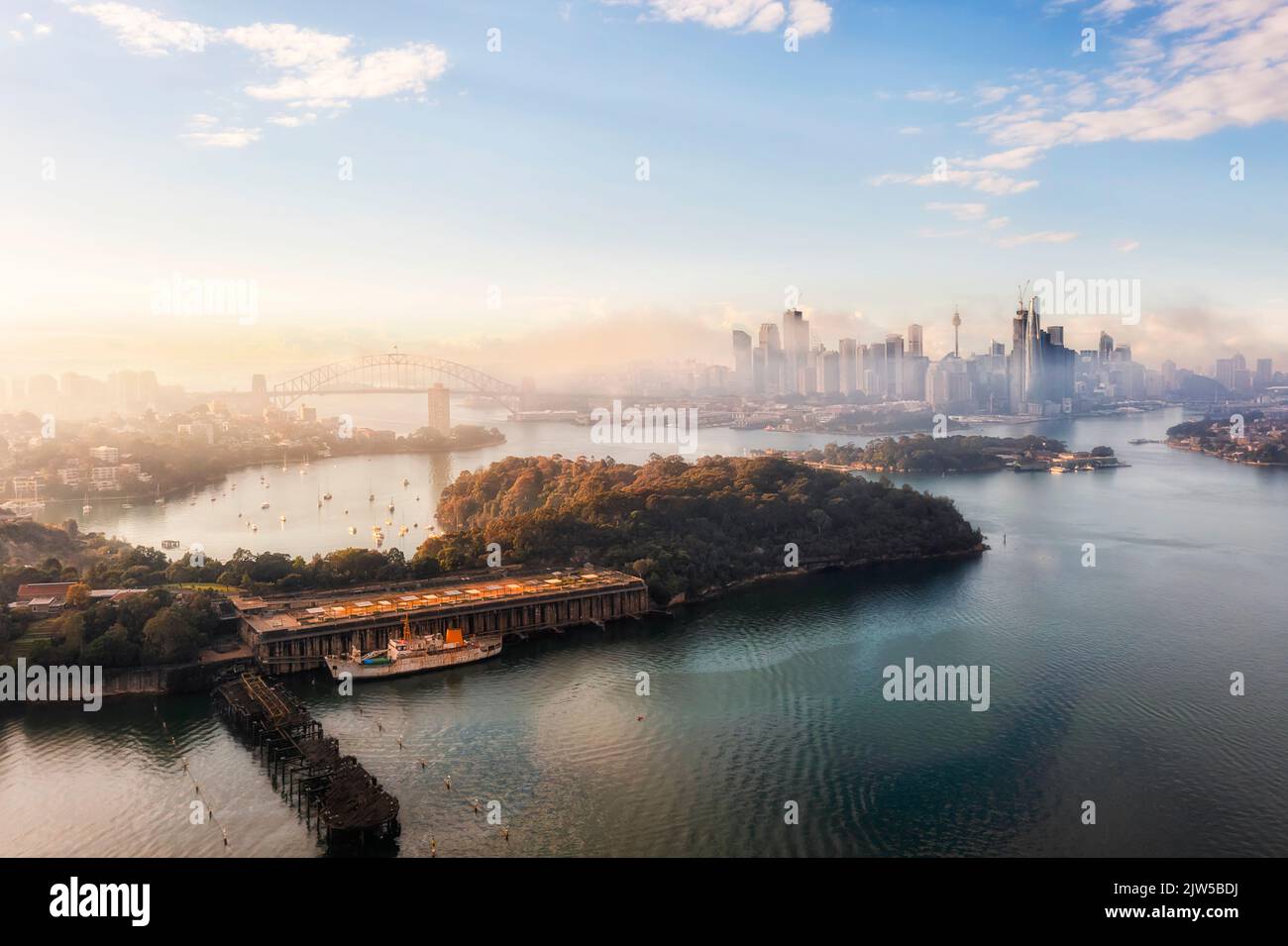 Balls Head reserve on Sydney harbour in view of City CBD landmarks in misty foggy morning - aerial cityscape. Stock Photo