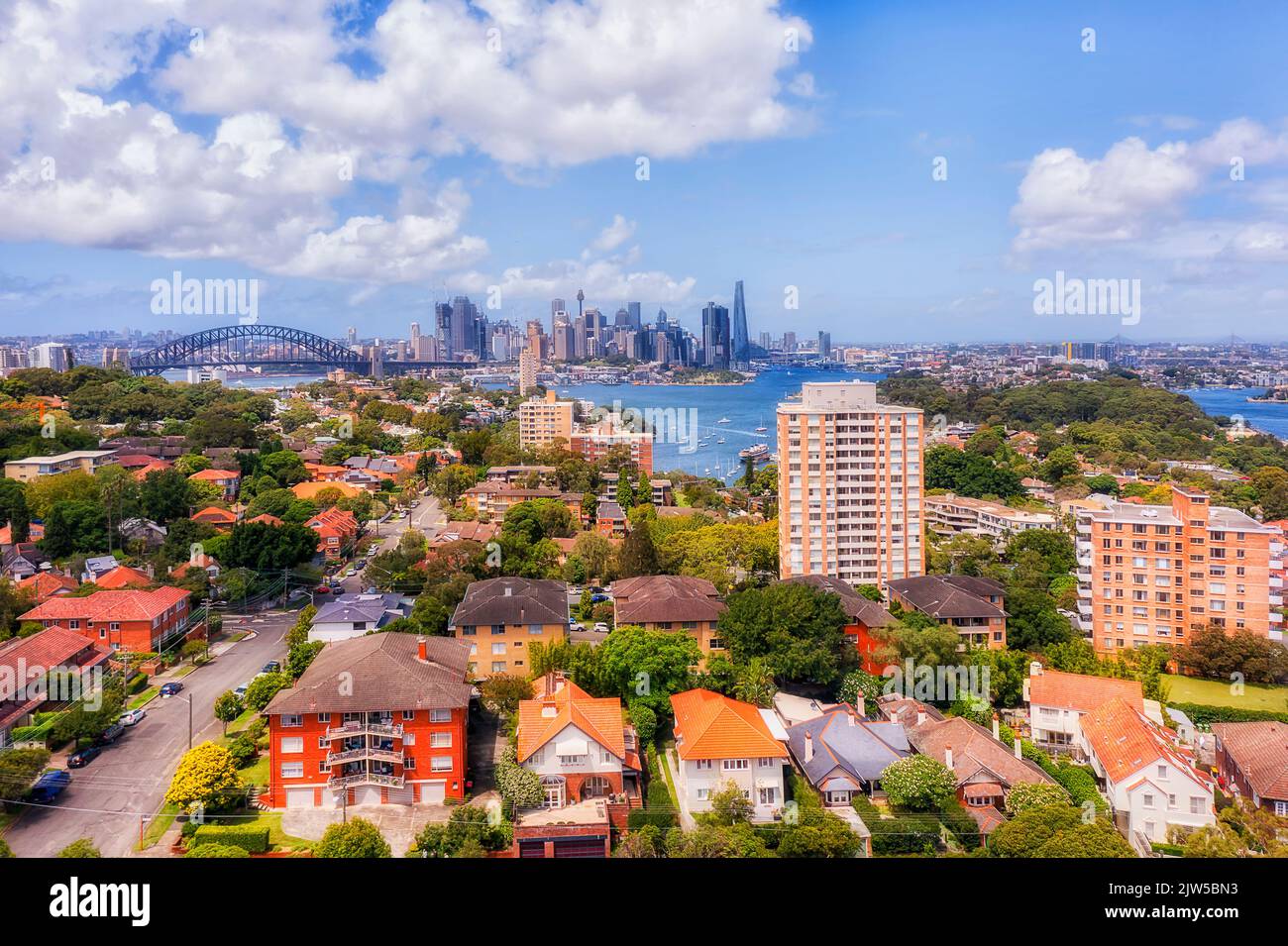 Local residential low-rise houses in green wealthy suburb of North Sydney in view of Sydney harbour bridge and city CBD landmarks - aerial cityscape. Stock Photo