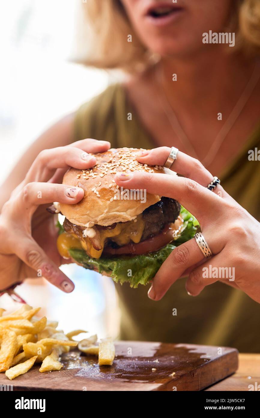 Hands holding a burger, on a restaurant table. Delicious and nutritious food. American style. Stock Photo