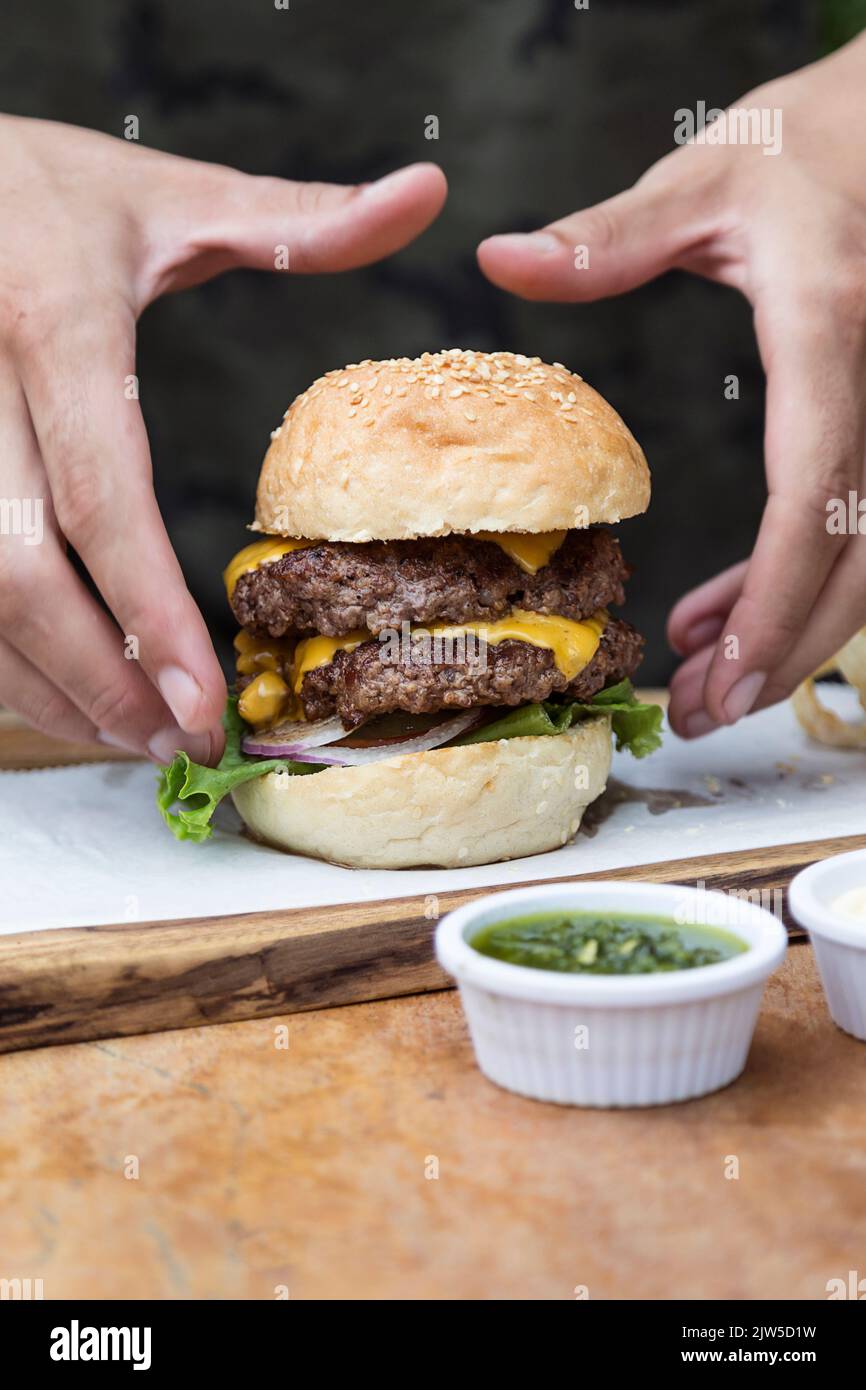 Hand holding a whole hamburger, on a restaurant table. Delicious and ...