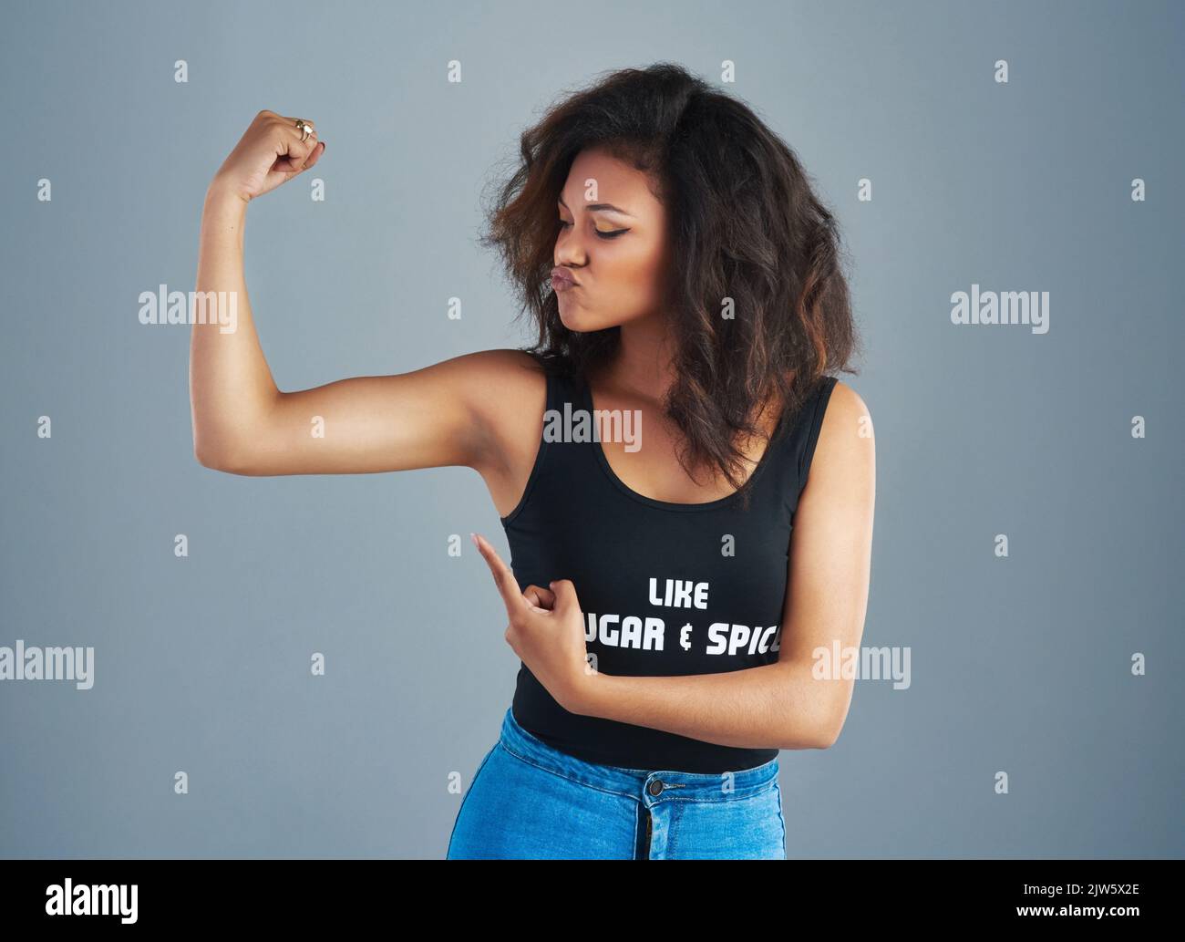 Check out those muscles. an attractive young woman posing against a gray background. Stock Photo