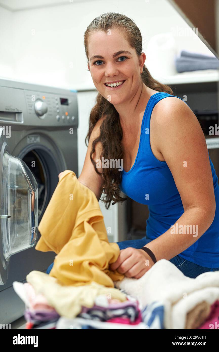 Sorting through some laundry. Portrait of a young woman busy with laundry at a washing machine. Stock Photo