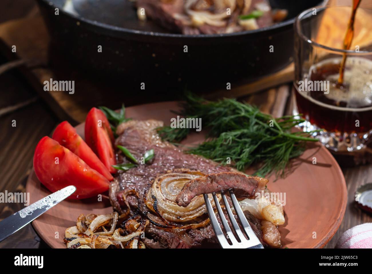 Two fried beef steaks.Focus on piece of meat strung on fork, beer poured into glass, selective focus.Healthy food concept. Stock Photo