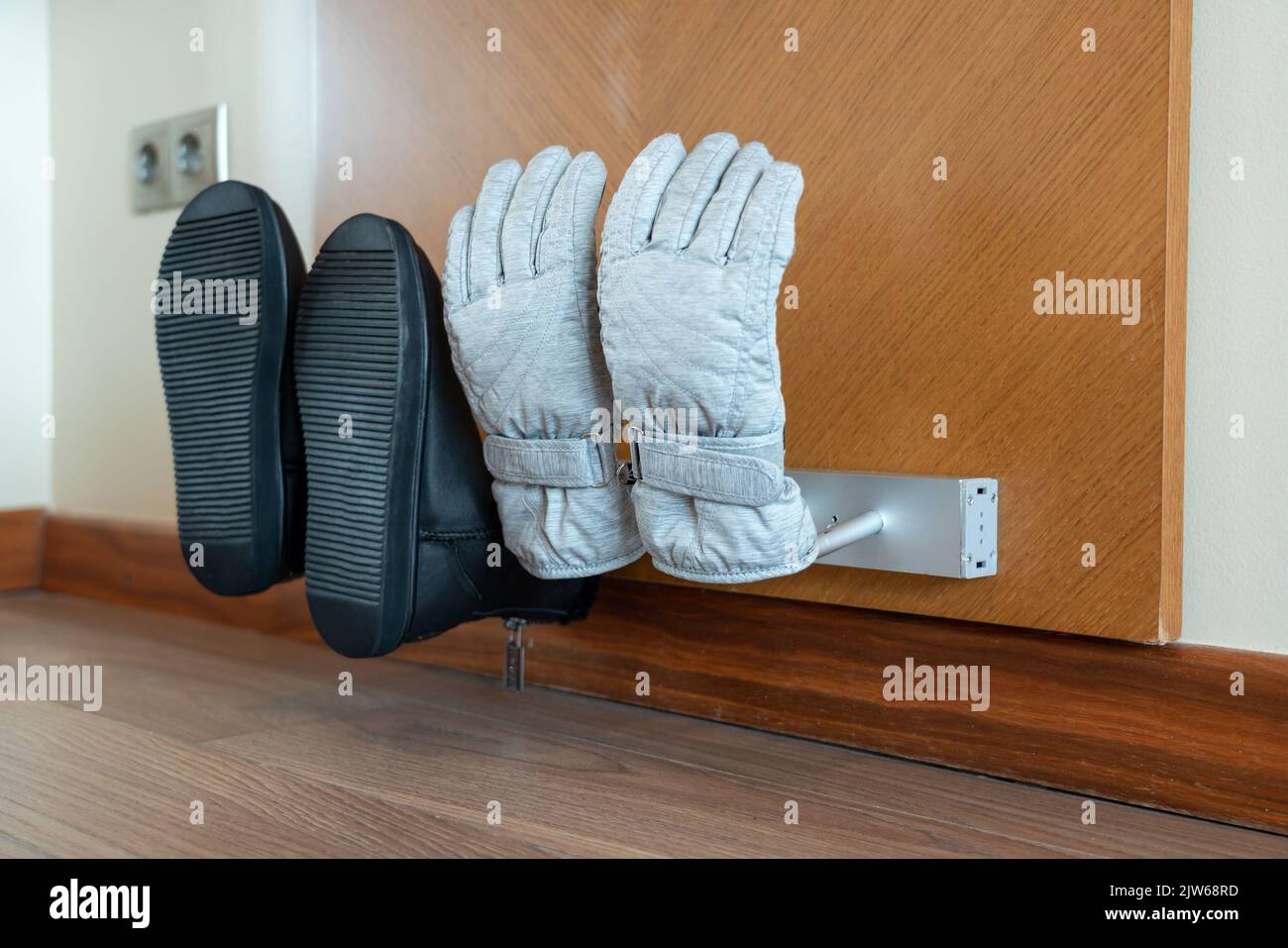 Wallmounted electric dryer with shoes and gloves put on it, side view