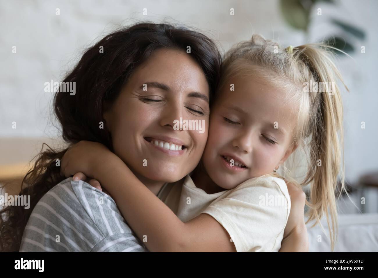Closeup happy Latina young mother strong cuddle little blonde daughter Stock Photo