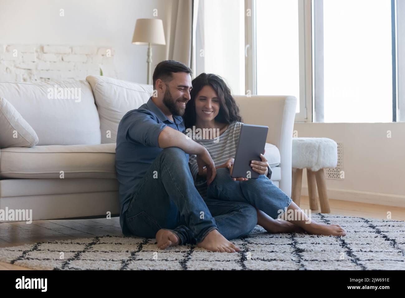 Millennial couple using digital tablet seated on floor at home Stock Photo
